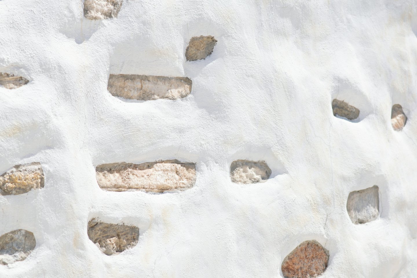 Du plâtre blanc rugueux recouvre des pierres texturées beiges et brunes.