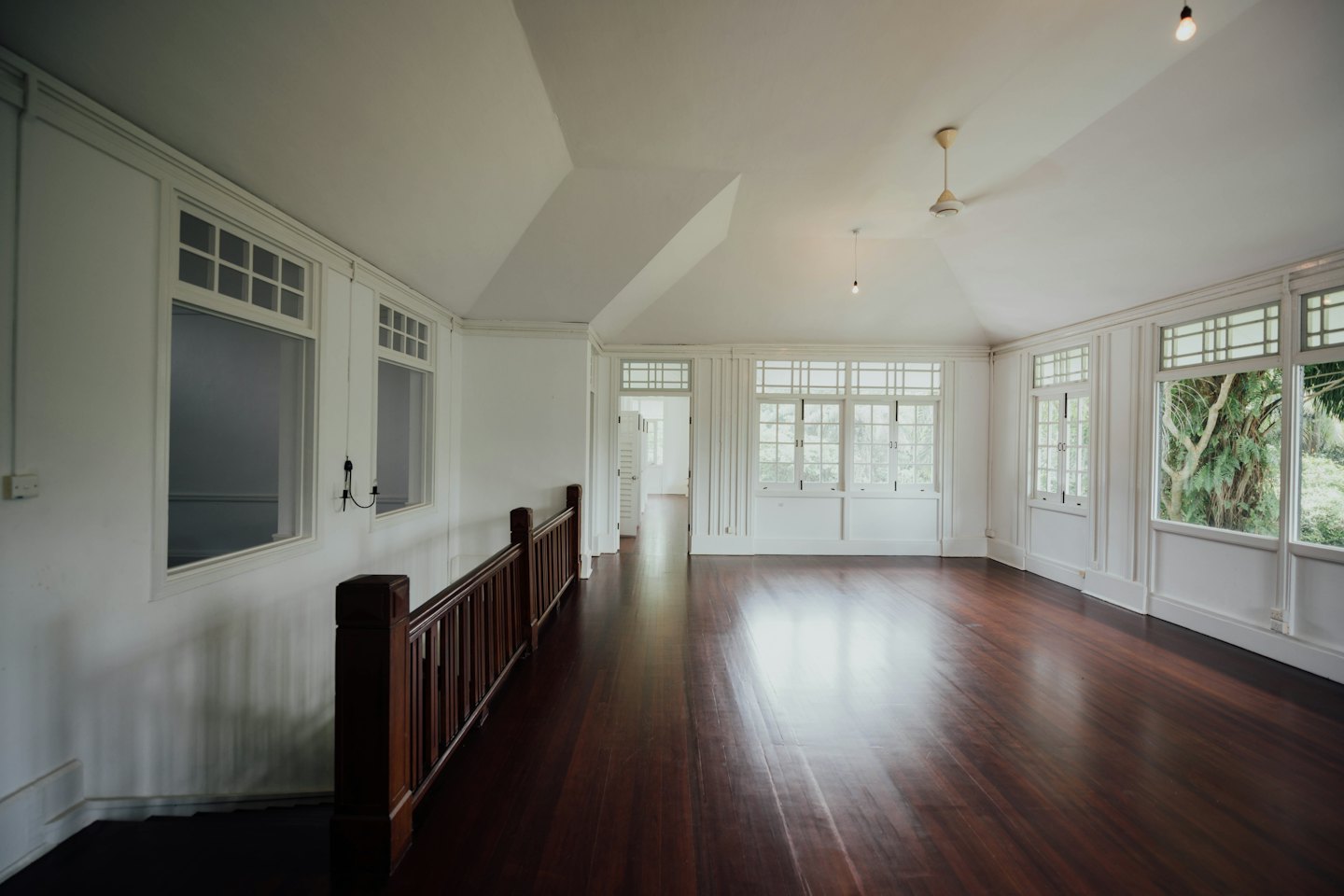 Chambre vide avec parquet poli et grandes fenêtres à croisillons.