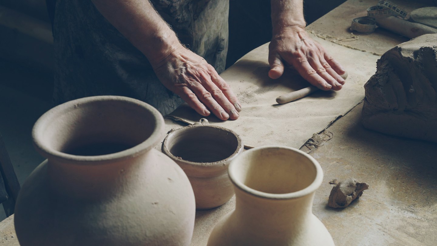 Un artisan façonne un pot en argile sur un établi recouvert de papier.